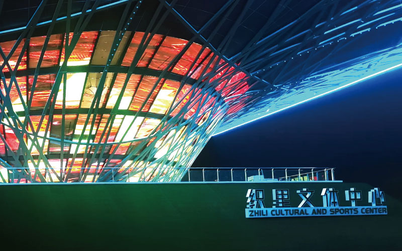 位于浙江湖州的織里文體中心，是一座大型異形鋼架結(jié)構(gòu)建筑。三思為其定制近1000平米透明屏，運(yùn)用高清LED透明屏及控制系統(tǒng)，將其打造成了一幅巨型建筑媒體立面。